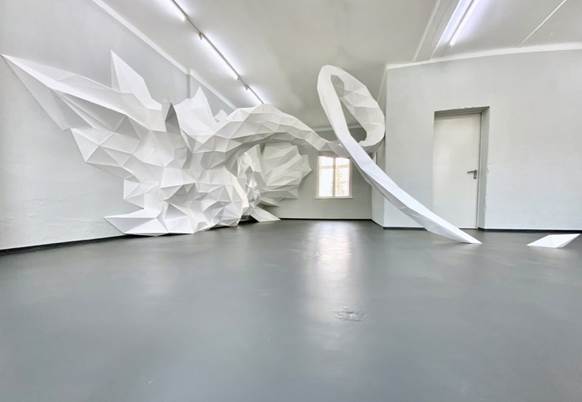 Ein weißer Raum, in dem ein großes Papierkonstrukt aus der Wand kommt